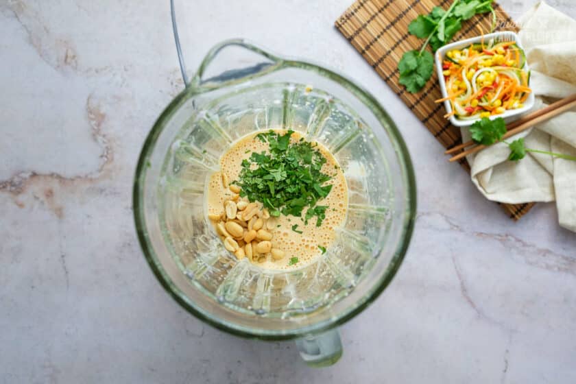 Thai peanut dressing ingredients in a blender plus cilantro and peanuts