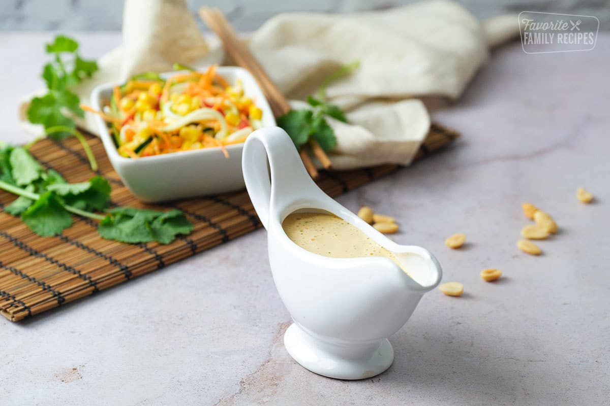 Thai peanut dressing in a pouring container with salad a peanuts