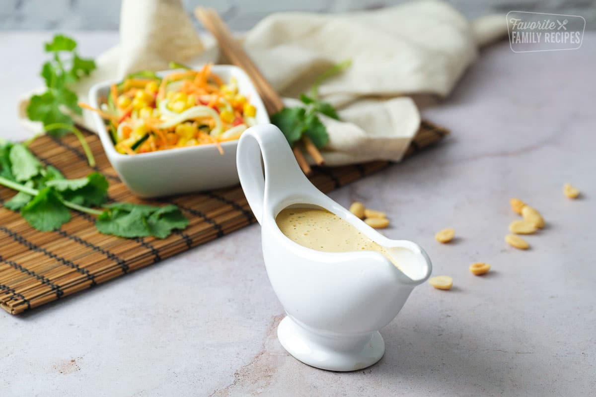 Thai peanut dressing in a pouring container with salad a peanuts.