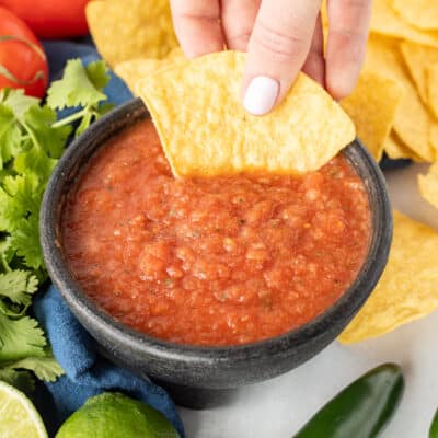 Hand dipping a tortilla chip into a bowl of Chili's Salsa.