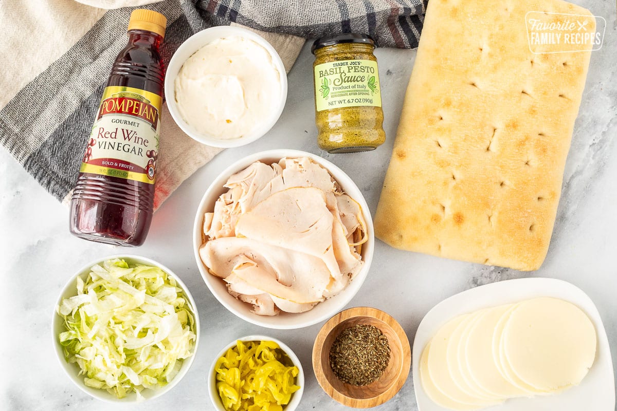 Ingredients to make Turkey Over Italy including focaccia bread, pesto sauce, mayo, red wine vinegar, turkey breast, oregano, peperoncini, provolone cheese and lettuce.