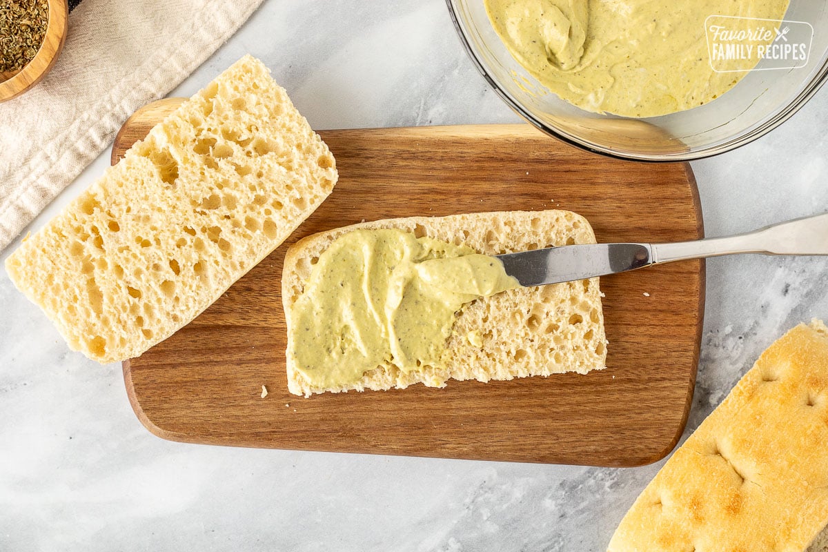 Spreading pesto mayo with a knife on focaccia bread.