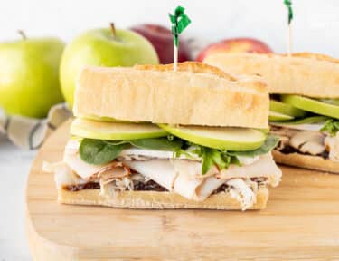 Two halves of Turkey Sandwich with Brie Cheese and Apples on a cutting board.