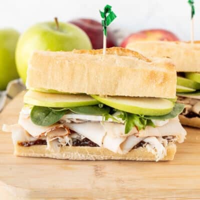 Two halves of Turkey Sandwich with Brie Cheese and Apples on a cutting board.
