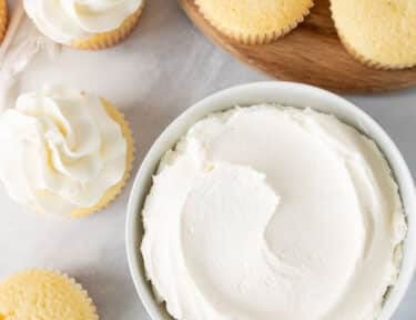 Bowl of Vanilla Buttercream Frosting with vanilla cupcakes.