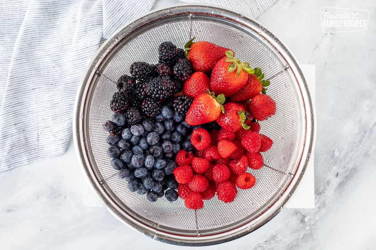 Colander with washed strawberries, raspberries, blackberries and blueberries.