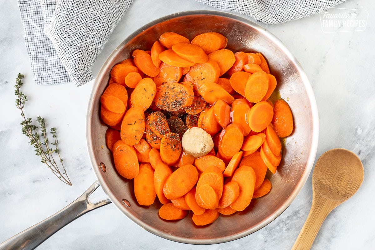 Thyme, honey, orange juice and brown sugar added to sauté carrots. Wooden spoon on the side.