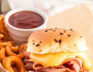 Arby's ham and cheddar melt inside a basket with curly fries and Arby's sauce.