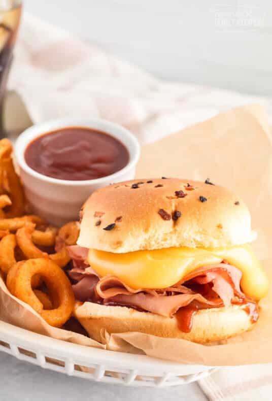 Arby's ham and cheddar melt inside a basket with curly fries and Arby's sauce.