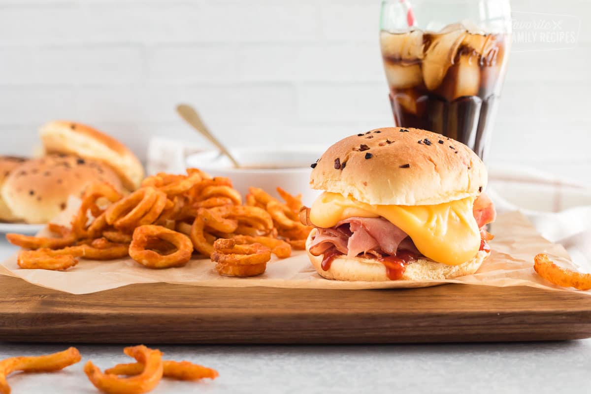 Arby's ham and cheddar melt on a board with curly fries and a glass of Coke