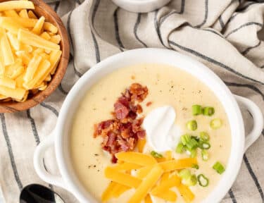 Instant Pot Loaded Potato Soup in a bowl with cheddar cheese, bacon, sour cream and green onions.
