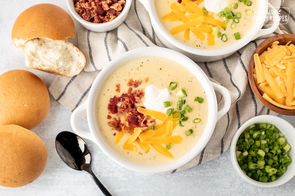 Two bowls of Instant Pot Loaded Potato Soup with bacon, sour cream, green onions and cheddar cheese. Rolls on the side.