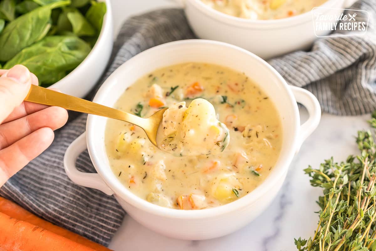 A bowl of chicken gnocchi soup with a spoon taking a bite