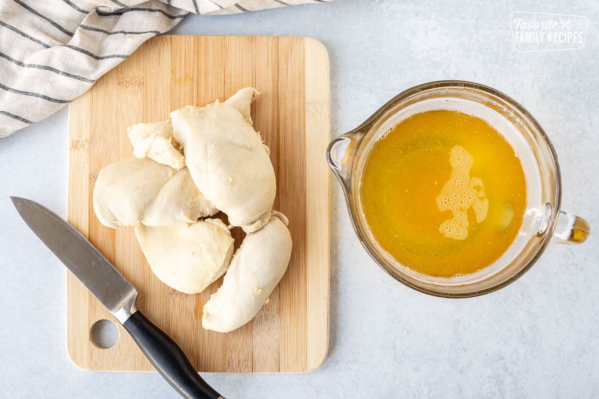 Cutting board with cooked chicken breasts next to a bowl of chicken broth.