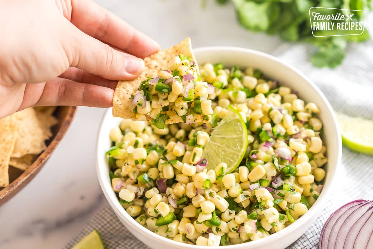 A tortilla chip being dipped in corn salsa