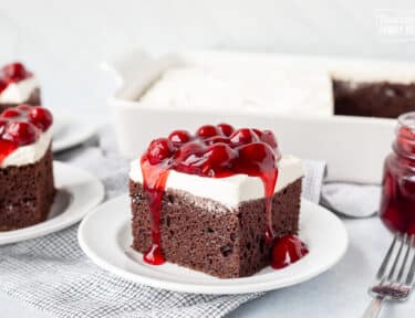 Chocolate Cake slice with Cherry topping on a plate with the cherry dripping from the sides.