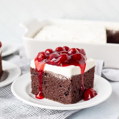 Chocolate Cake slice with Cherry topping on a plate with the cherry dripping from the sides.