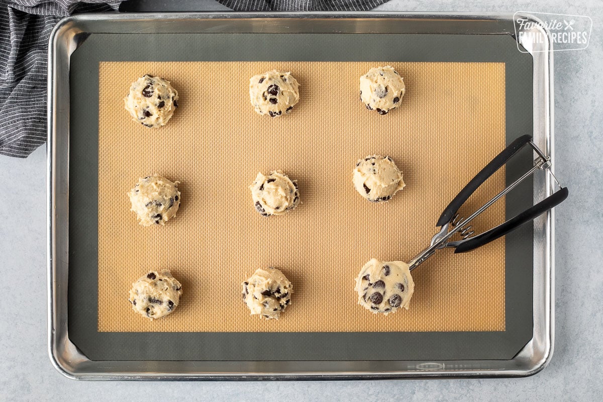 Cookie sheet with scooped balls of chocolate chip cookie dough with a cookie scoop.
