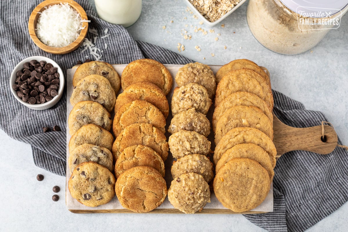 Variety of cookies lined up on a board. Variety includes chocolate chip cookies, snickerdoodle cookies, banana coconut and peanut butter cookies.