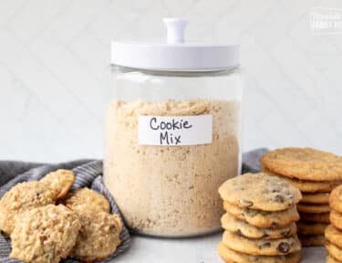 Canister of Cookie dough mix next to stacks of baked cookies.