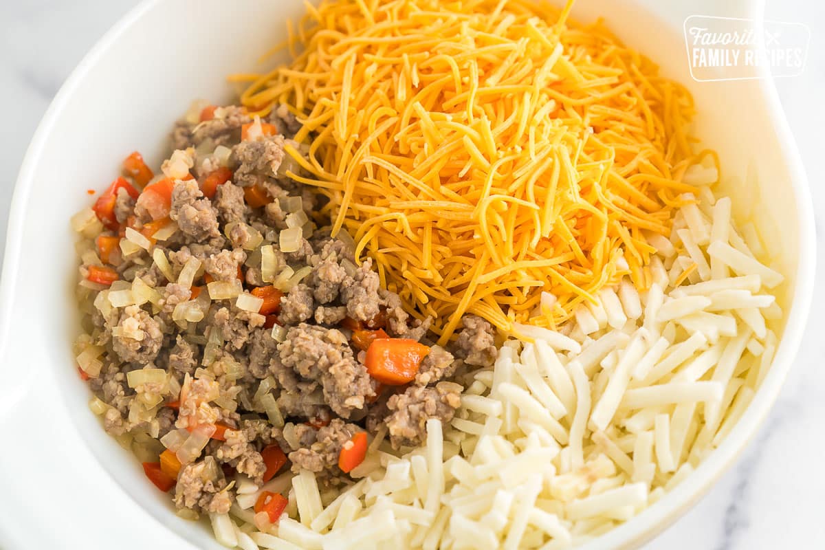 Sausage, peppers, onions, shredded cheese, and frozen hash browns in a bowl