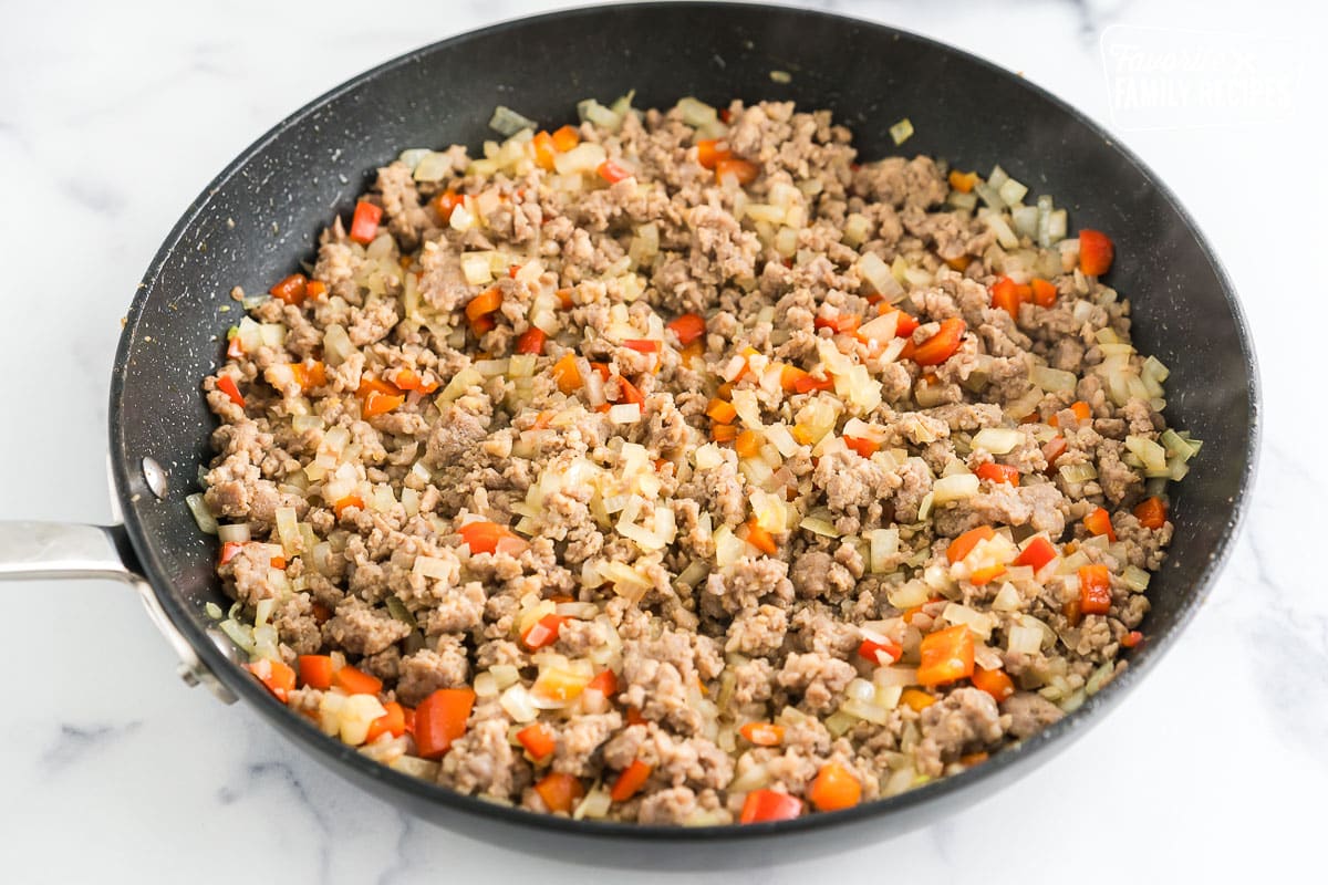 ground sausage, peppers, and onions cooking in a skillet