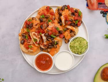 Overhead shot of Oven Nachos on a plate with guacamole, sour cream, and salsa