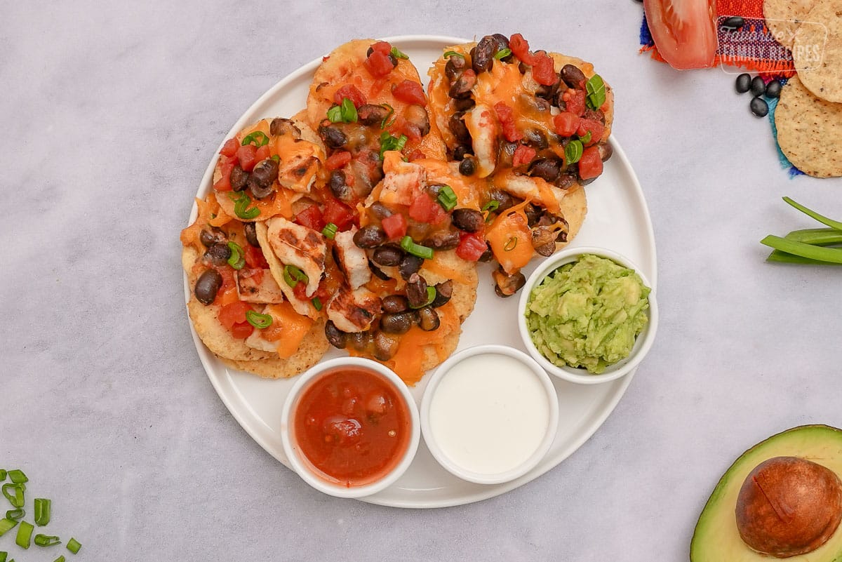 Overhead shot of Oven Nachos on a plate with guacamole, sour cream, and salsa