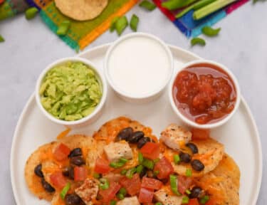 Tall image of Oven Nachos on a plate with guacamole, sour cream, and salsa