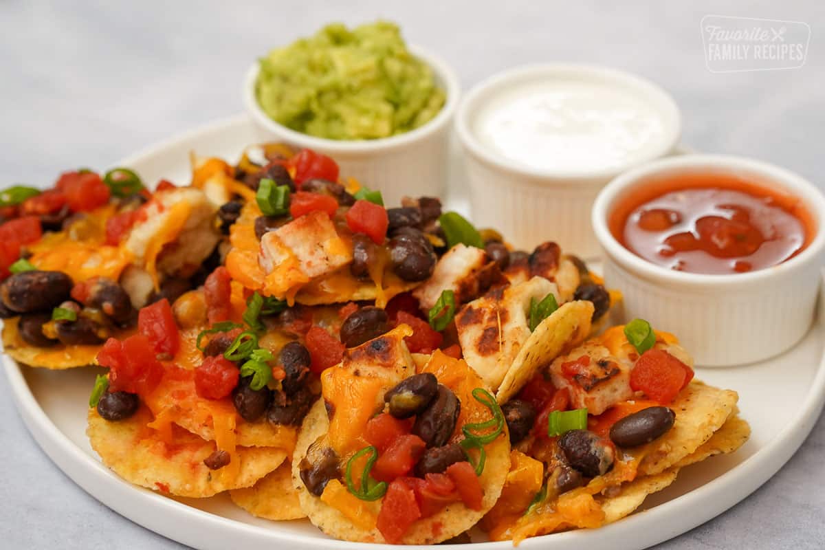 Side view of Oven Nachos on a plate with guacamole, sour cream, and salsa