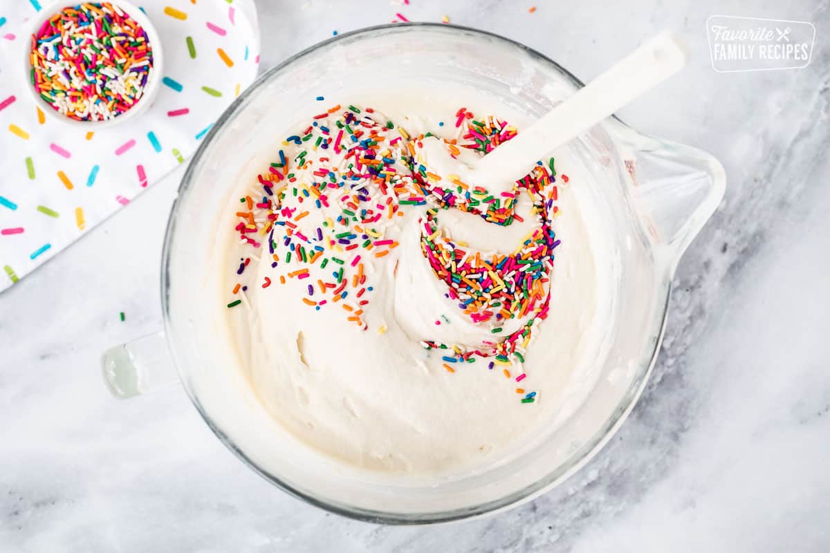 Mixing bowl with spatula combining batter and sprinkles.