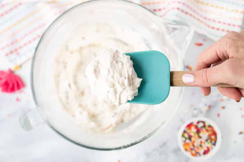 Spatula holding scoop of Funfetti frosting over a mixing bowl.