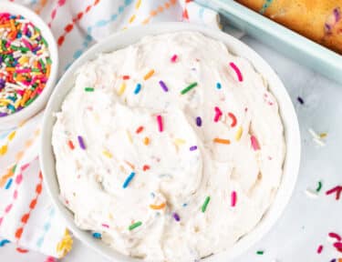 Bowl of Funfetti frosting with sprinkles and cake on side.