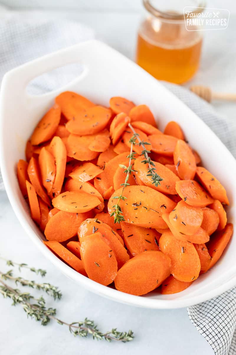 Glazed carrots in a serving dish with fresh thyme as garnish.