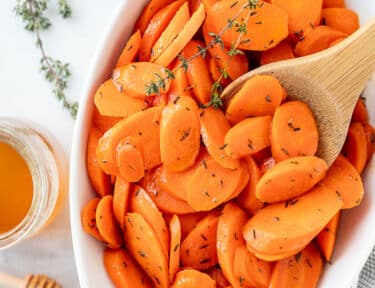 Glazed carrots in a serving dish with a wooden spoon.