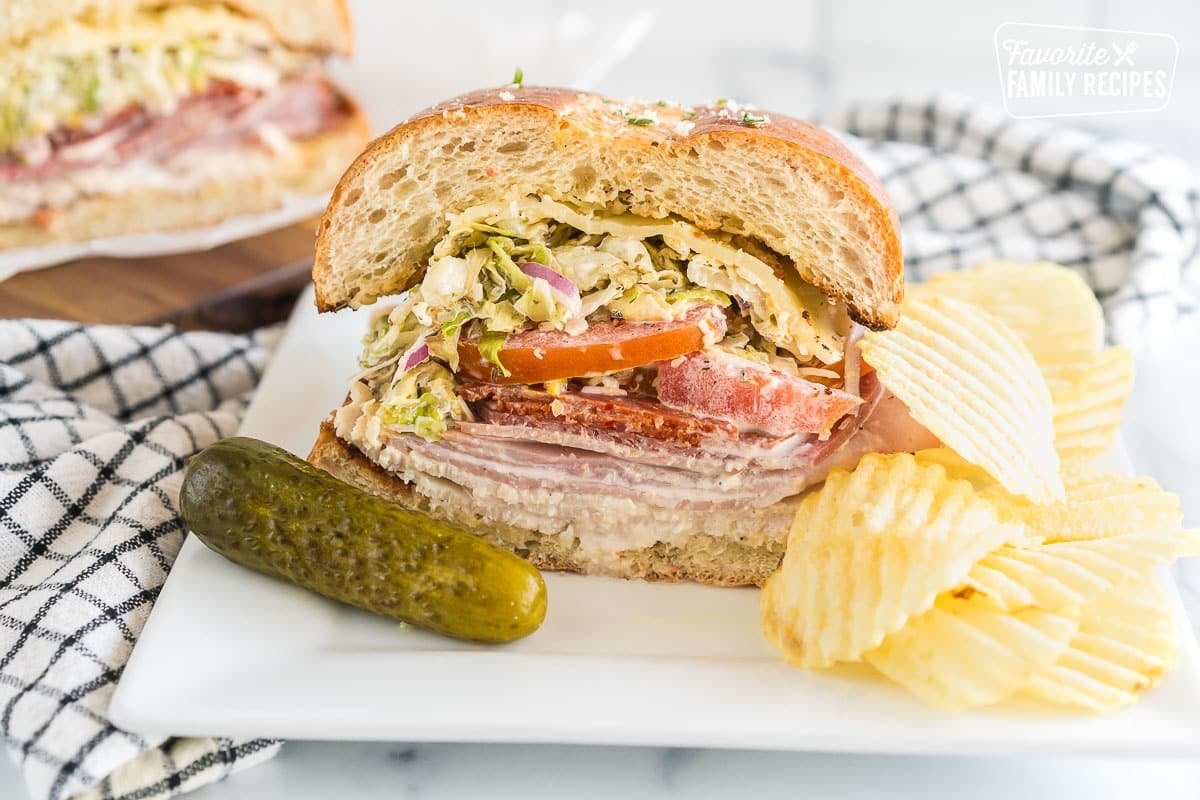 A slice of a Grinder sandwich on a plate with chips and a pickle.