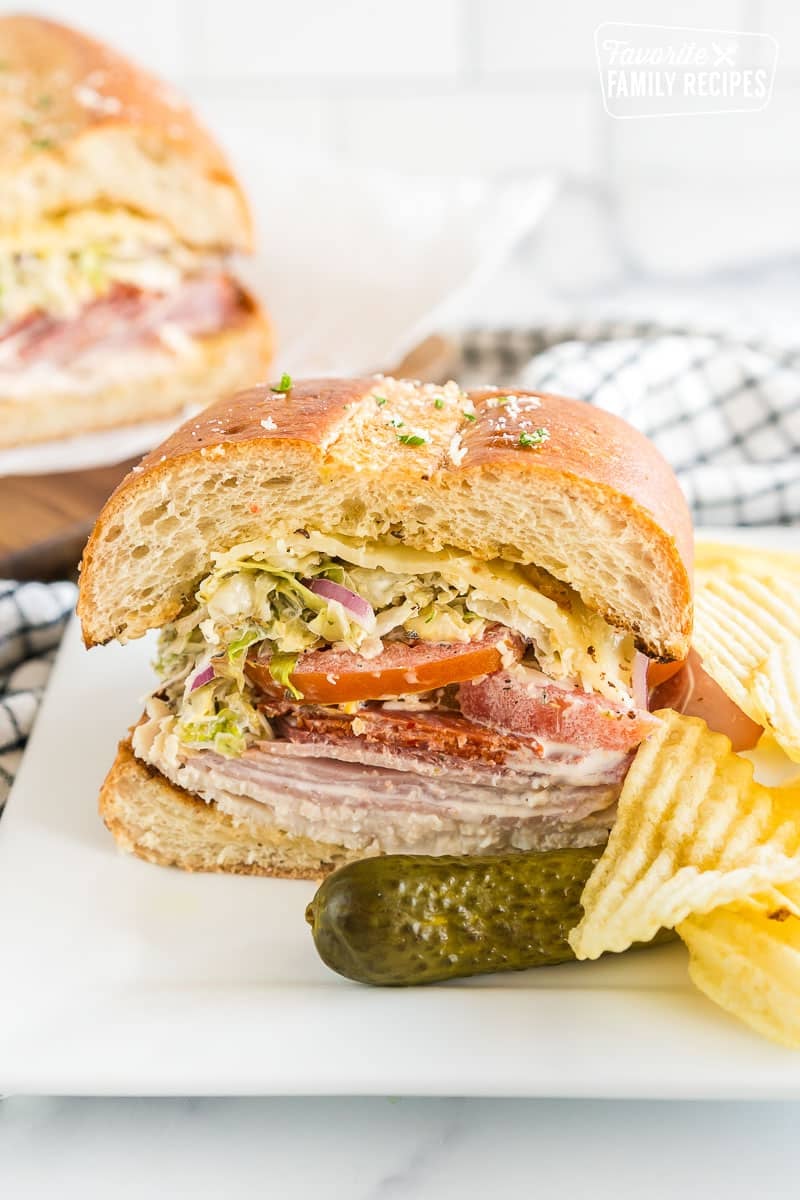 A slice of a Grinder sandwich on a plate with chips and a pickle.