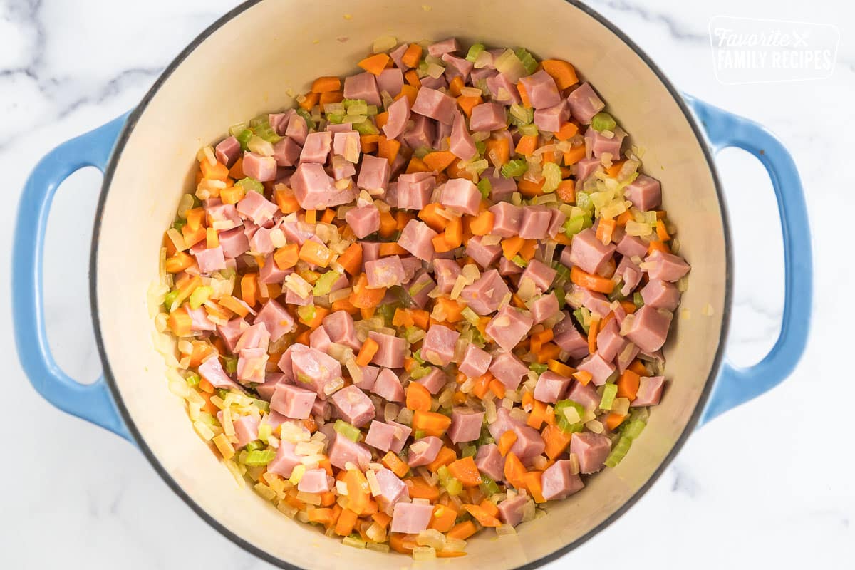 A large pot with ham, carrots, onions, and celery
