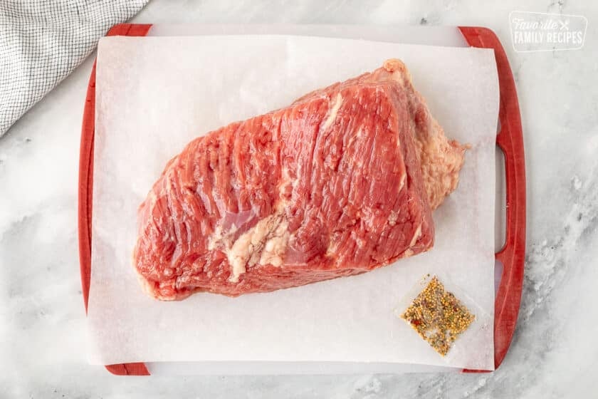 Cutting board with a raw corned beef brisket and a seasoning packet.