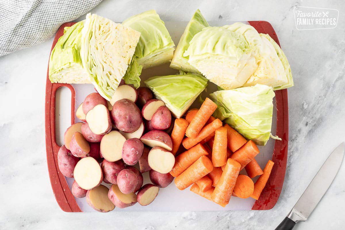 Cutting board with cut up cabbage, potatoes and carrots. Knife on the side.