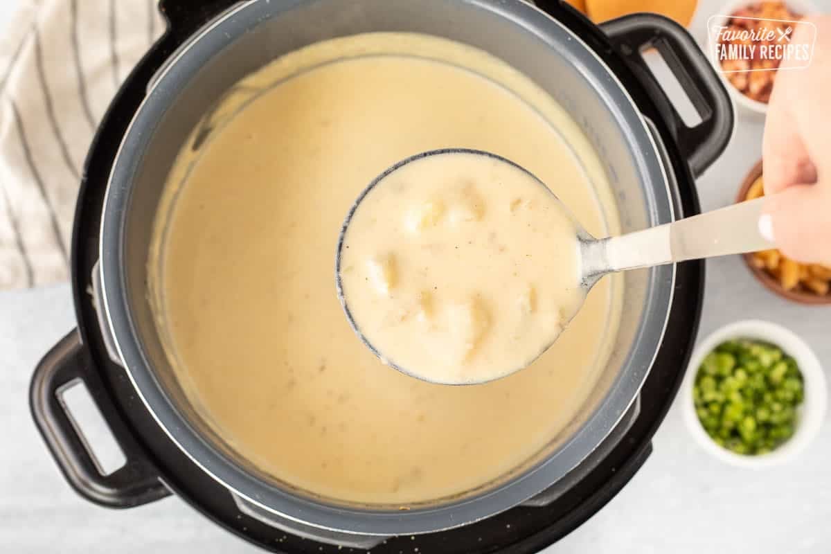 Ladle with cooked Instant Pot Loaded Potato Soup. Green onions, cheese and bacon on the side.