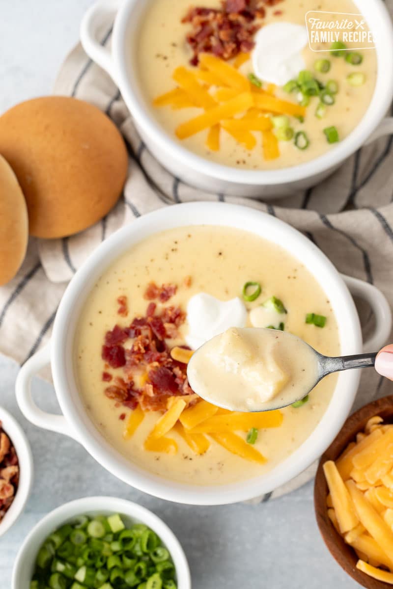 Spoon holding Instant Pot Loaded Potato Soup with bacon, sour cream, green onions and cheddar cheese.
