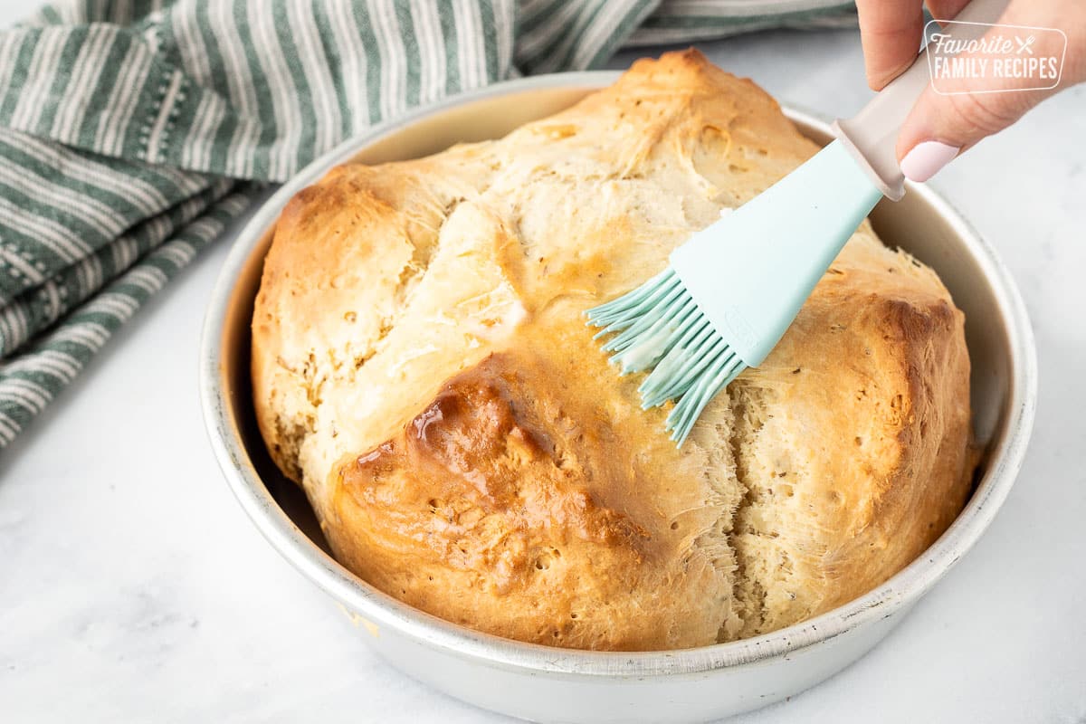 Baked Irish Soda Bread in a pan with a pastry brush spreading butter.