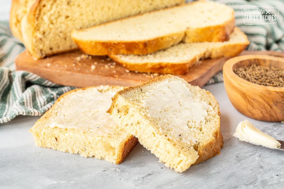 Two slices of Irish Soda Bread with butter on top. Bowl of caraway seeds on the side.