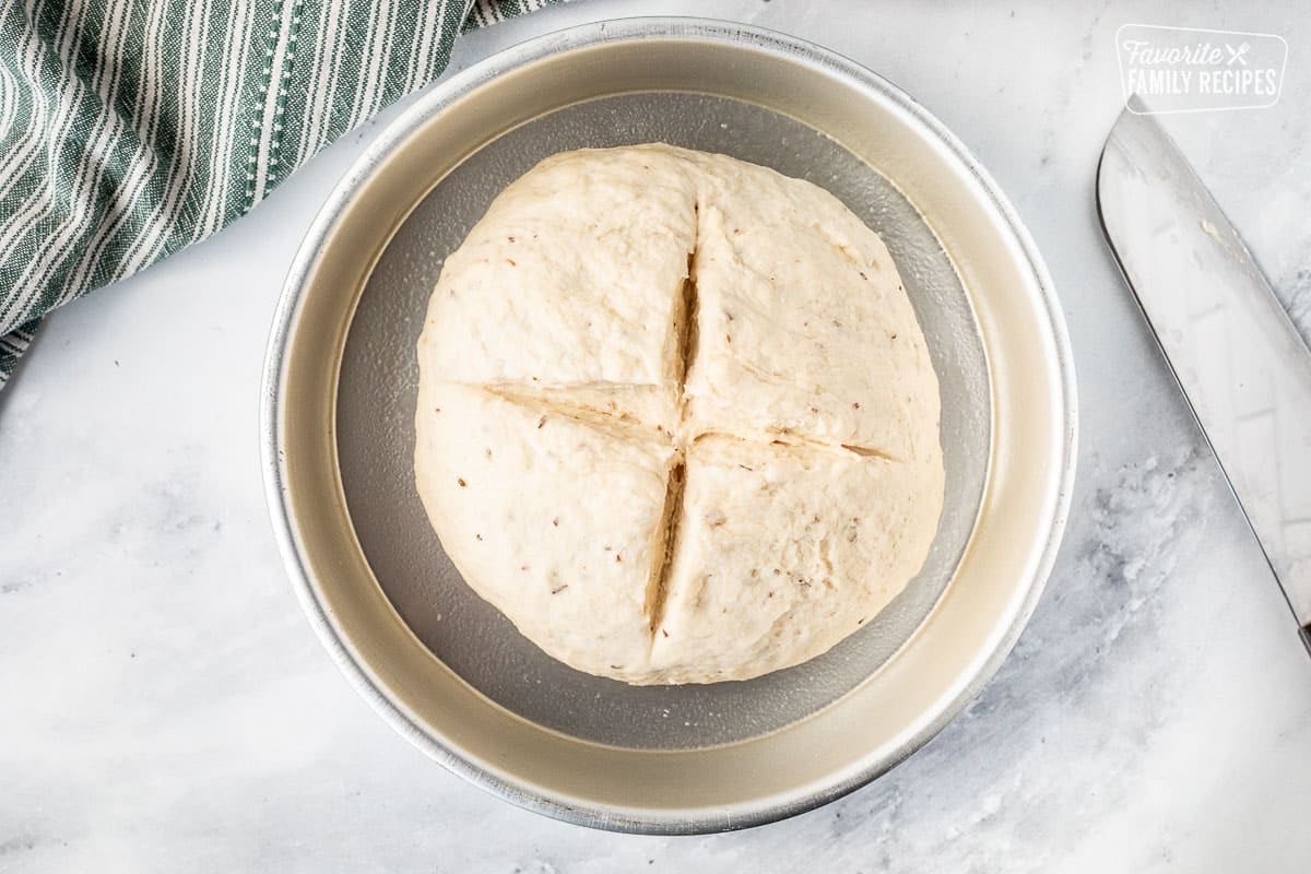 Slits cut into a ball of Irish Soda Bread dough in a cake pan. Knife on the side.