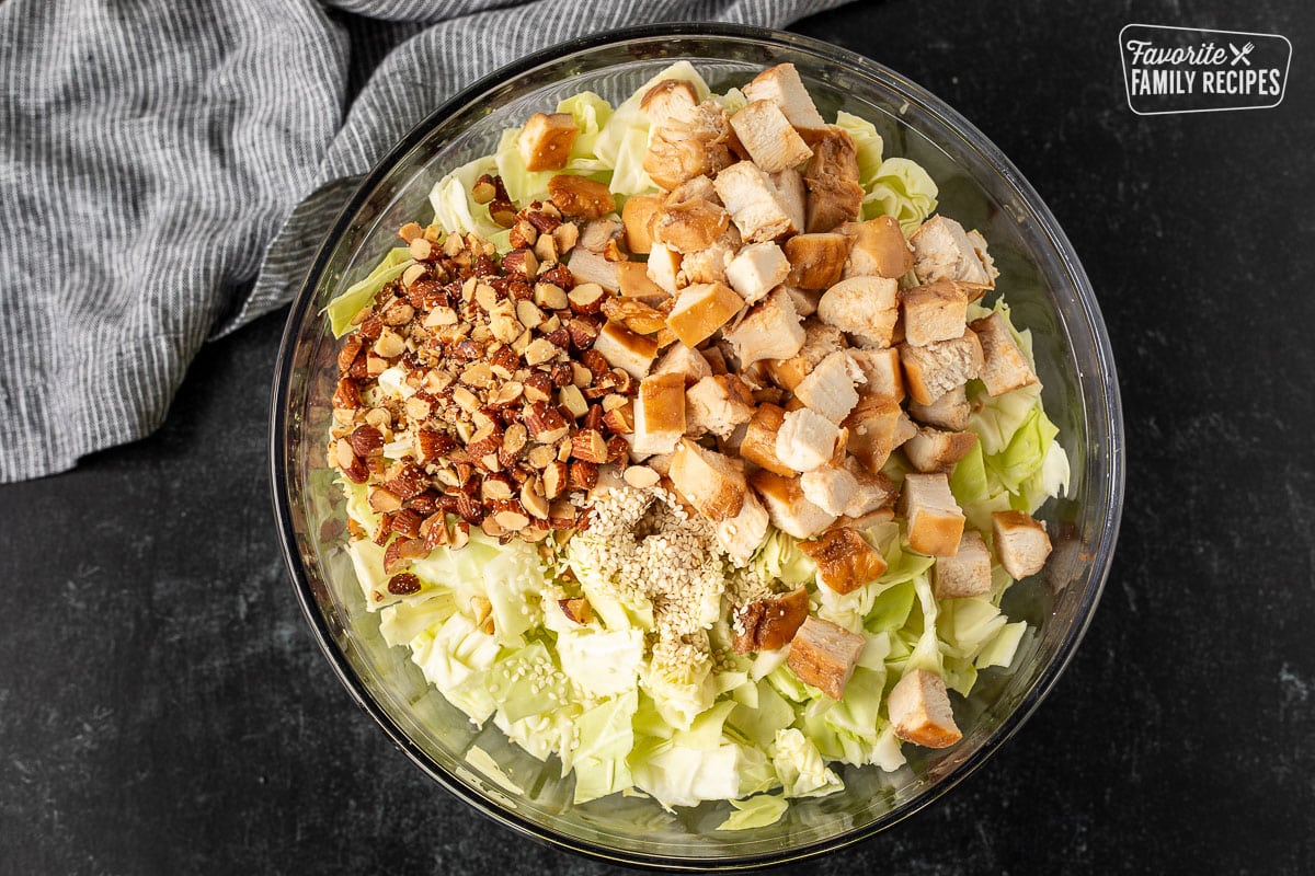 Bowl of cabbage, cut teriyaki chicken, chopped almonds and sesame seeds.