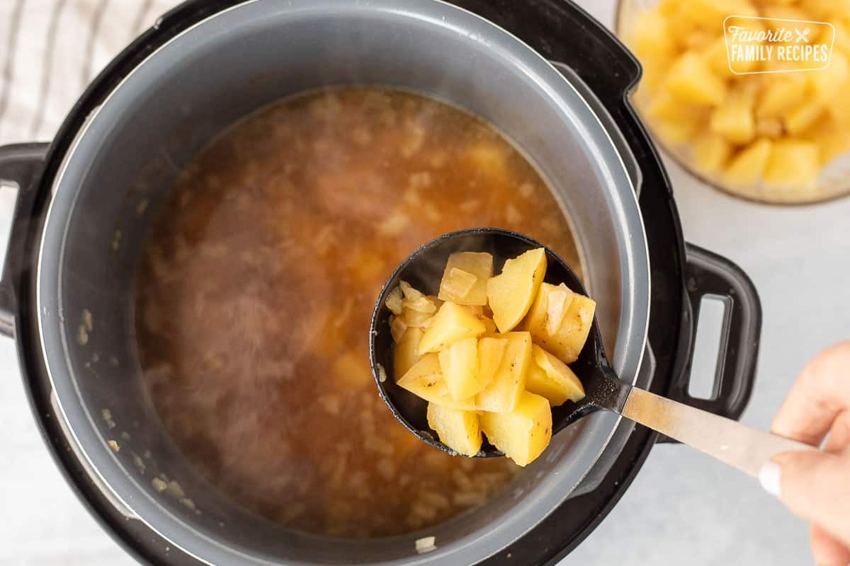 Ladle scooping cooked potatoes from broth into bowl.