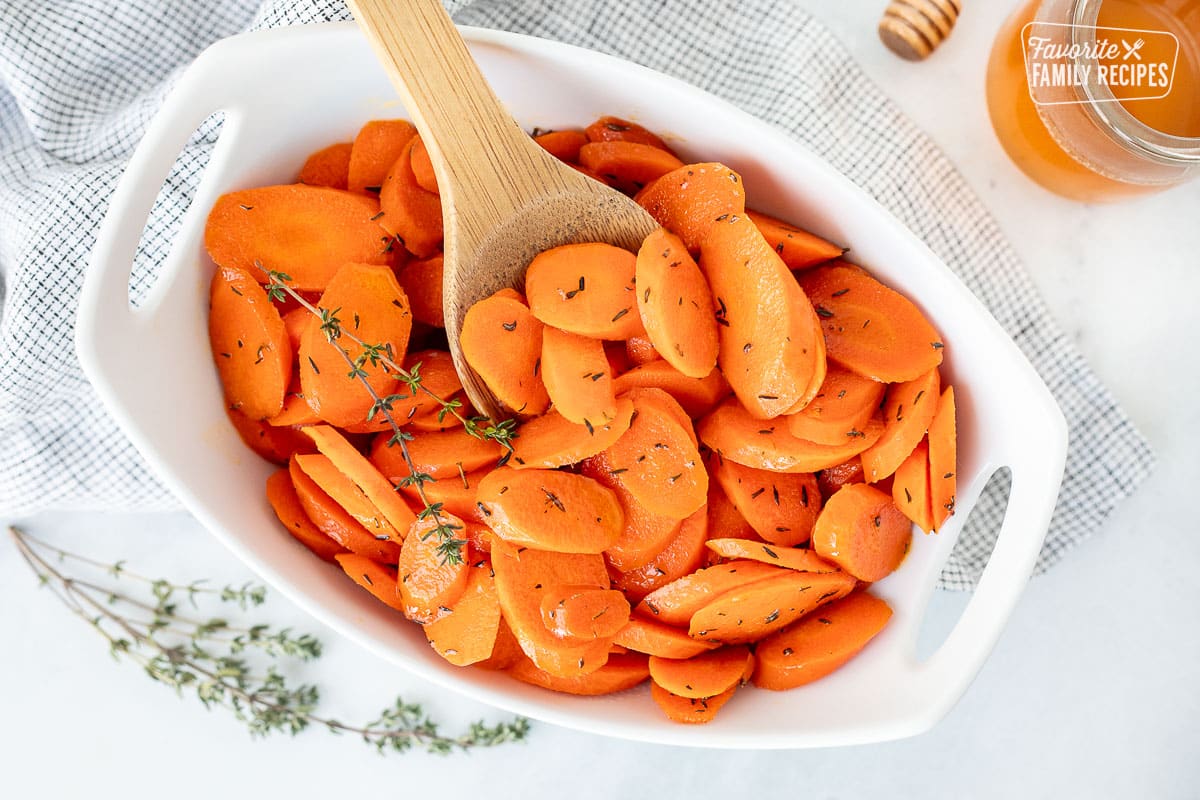 Serving dish with honey glazed carrots and a wooden spoon.