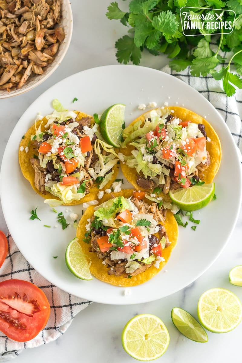 Shredded Pork Tostadas are easy and so flavorful! Tender pork is made in a slow-cooker and the tortillas are baked, not fried, making this a light, delicious meal. Three shredded pork tostadas on a plate
