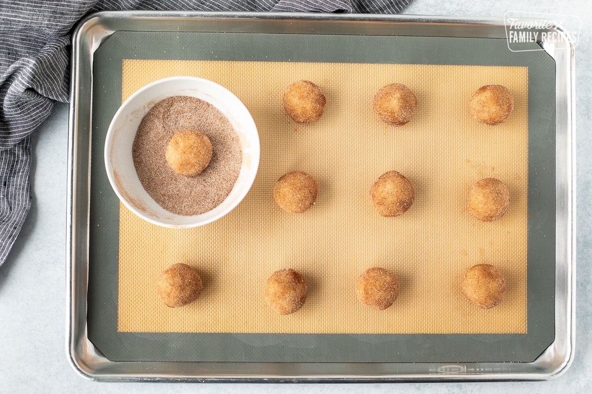 Cookie sheet with a bowl of cinnamon sugar and balls of snickerdoodle cookie dough mix.